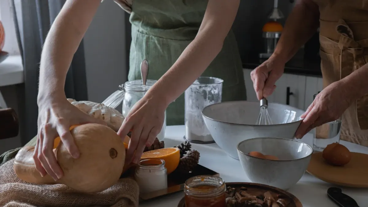 A dog owner spooning canned pumpkin over kibble in a stainless steel bowl